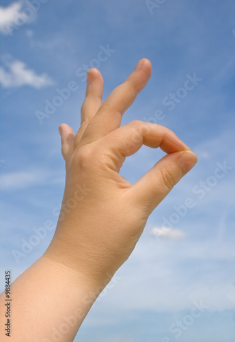 Human hand making OK sign against blue sky