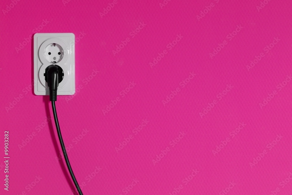 Cable connected into a power outlet on a pink wall Cable connected into a power outlet on a pink wall