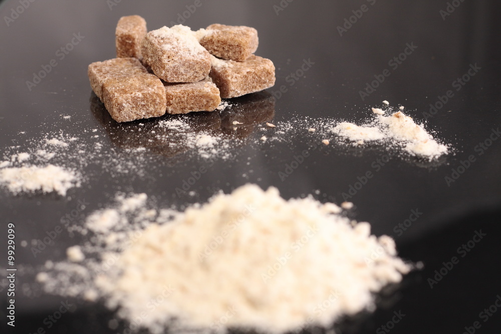 Brown sugar cubes and flour on black surface Brown sugar cubes and flour on black surface