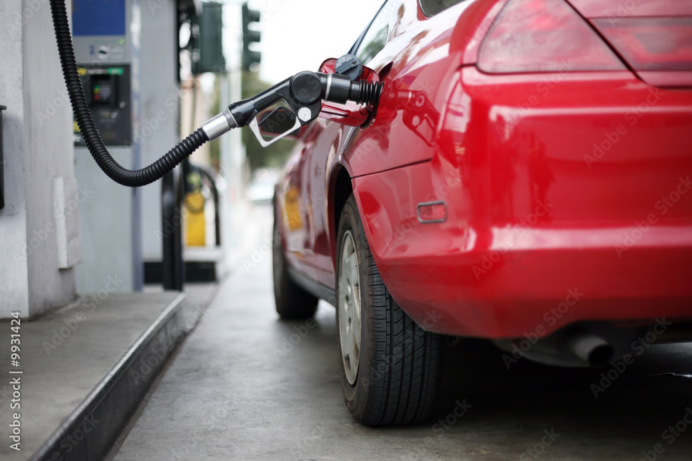 Fototapeta premium Red car at gas station being filled with fuel. Shallow DOF.