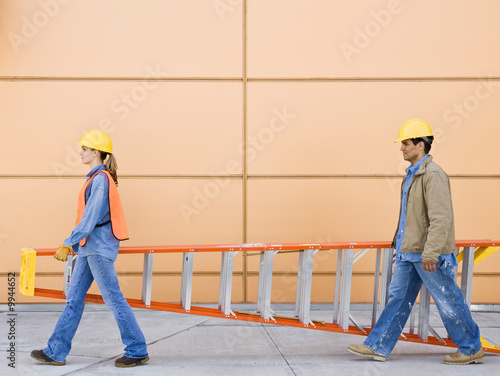 Side view of construction workers carrying ladder together