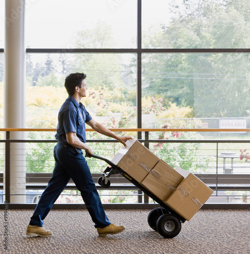 Delivery man in uniform pushing stack of boxes on dolly