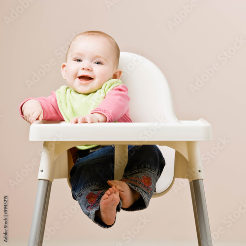 Happy, hungry baby in bib sitting in highchair