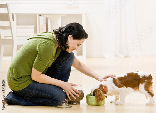 Devoted woman kneeling and feeding hungry pet dog
