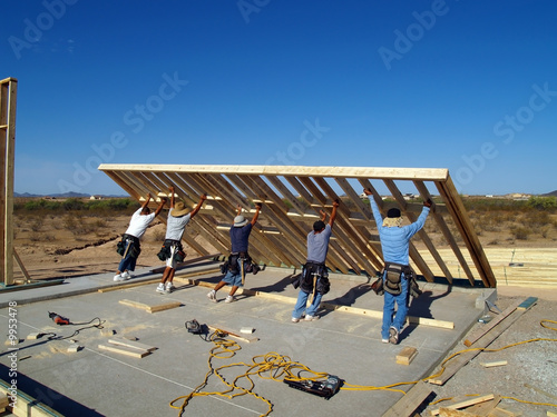 Construction workers lifting a wall frame into position.