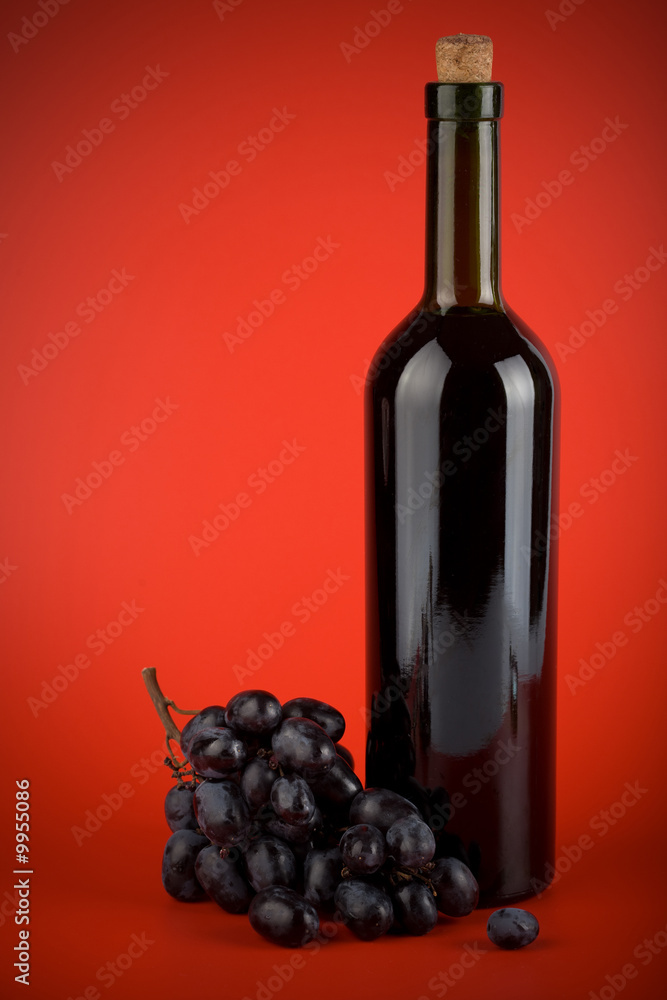 bottle of wine and grapes over red background