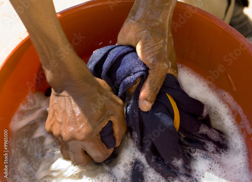 two african hands washing blue shirt in a red plastic tub