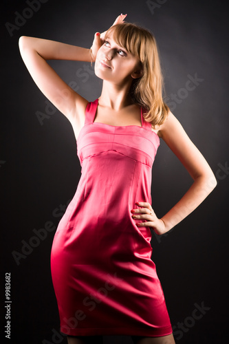 Young slim woman in pink dress. On dark background.