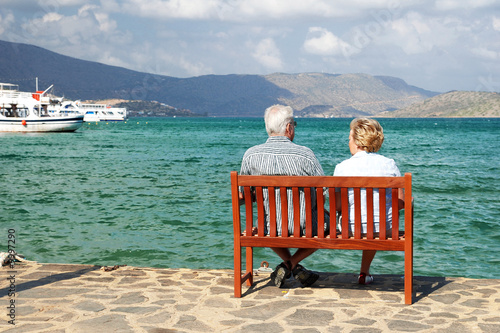 A man and a woman sitting on a bench and watching the sea