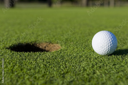 A white golf ball near the hole of a golfing green or course