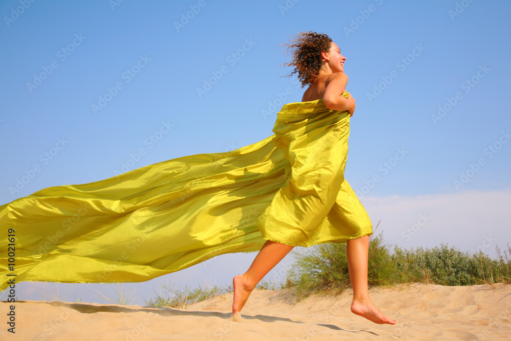 Young girl runs on sand in yellow fabric shawl