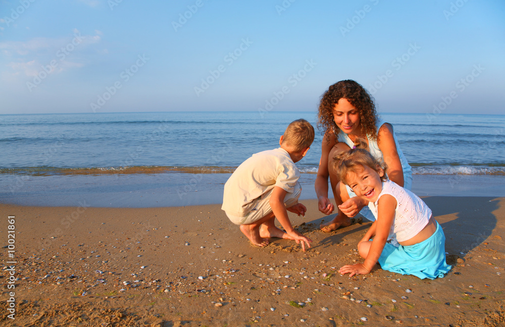Mother plays with children finding shells on sand at edge of sea