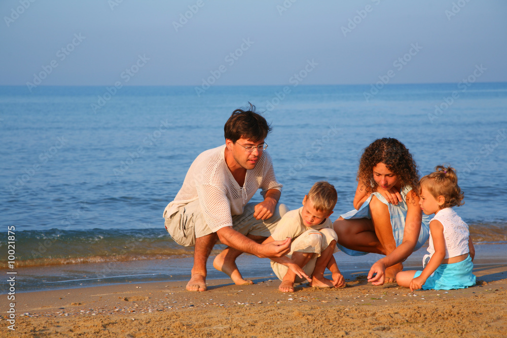 Parents play with children finding shells on sand at edge of sea