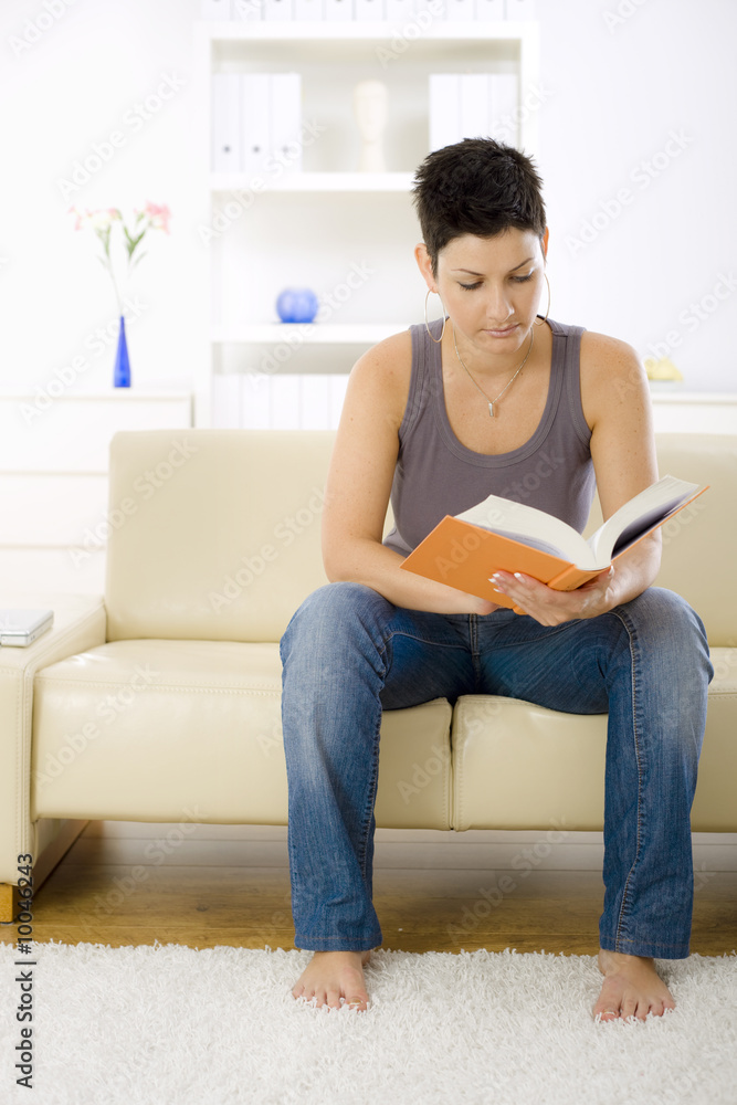Young woman reading book at home, sitting on sofa. Young woman reading book at home, sitting on sofa.