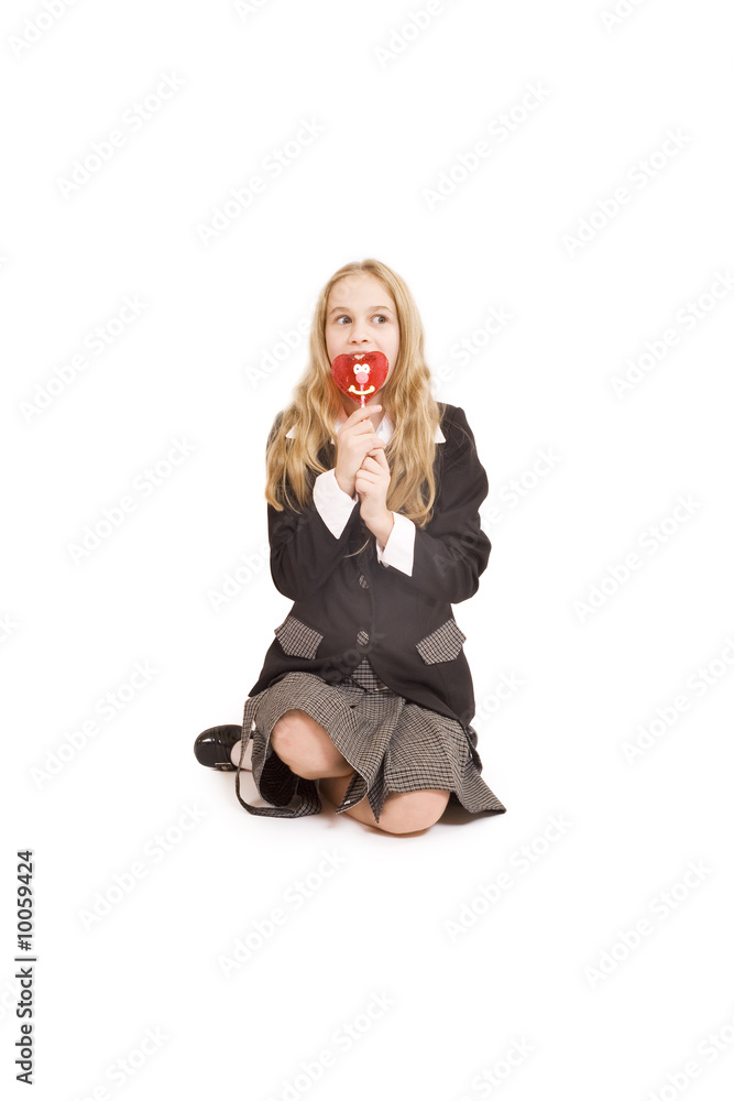 Fototapeta premium Schoolgirl and a heart shaped lolipop isolated on white
