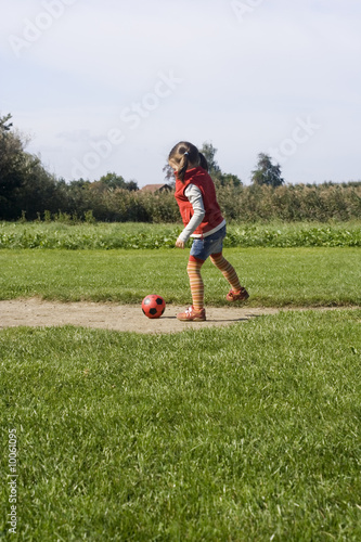 little girl playing football on the green field