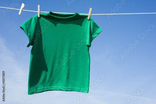 A green t-shirt hanging on a clothesline in front of a blue sky