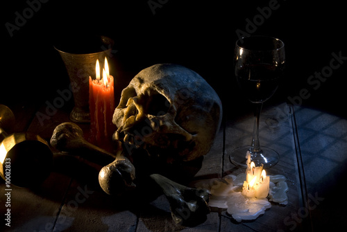 real skull and bones over a table, with candles and chalice.