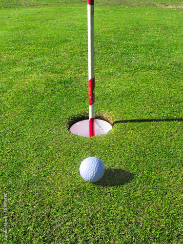 A golf ball lands near the hole on the green.