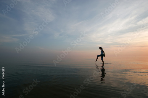 Silhouette of young woman wading in sea at sunset