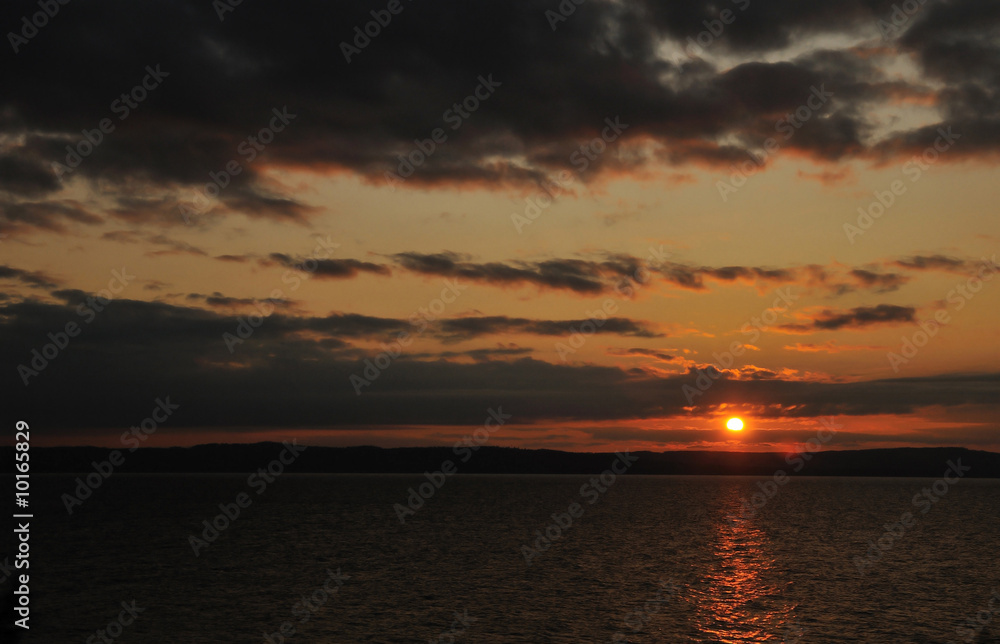The sun setting over a lake with a cloudy sky