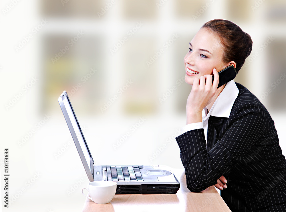 Young woman talking on a  phone and working on a laptop
