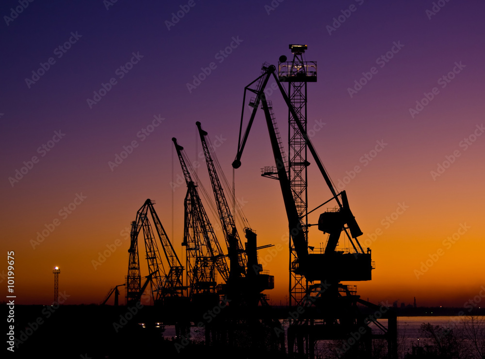 Silhouette of several cranes in a harbor, shot during sunset