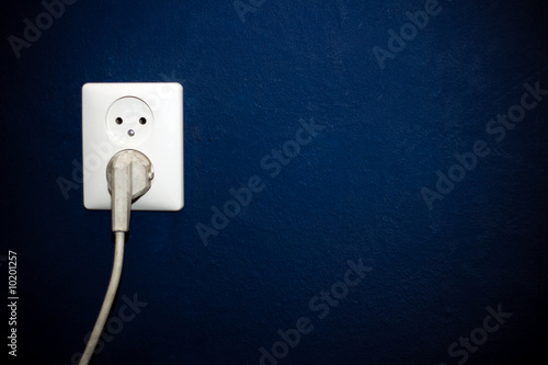 White socket with one old plug in dark blue wall