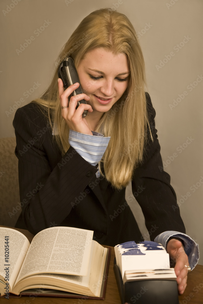 A young business woman talking on phone searching a Rolodex A young business woman talking on phone searching a Rolodex