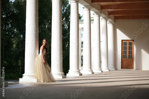 girl in white-golden gown of the bride amongst colonnades