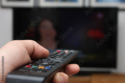 Human hand holding a remote control poined at flat screen tv