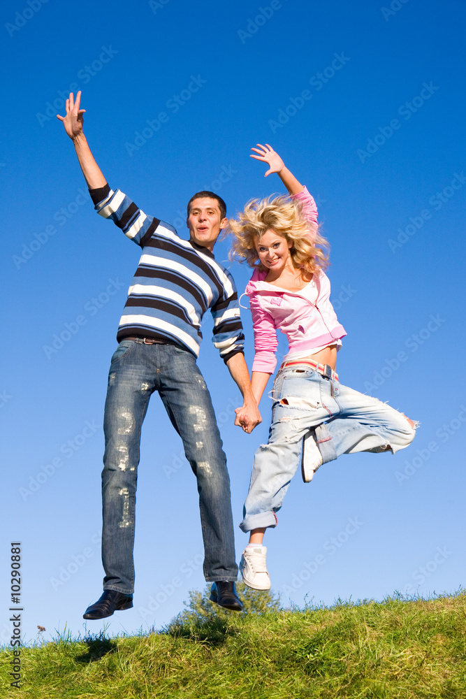 Happy young couple jumping in sky above a green meadow Happy young couple jumping in sky above a green meadow