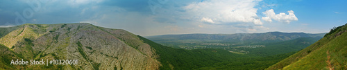 Mountain with clouds at horizont and green hils in front of