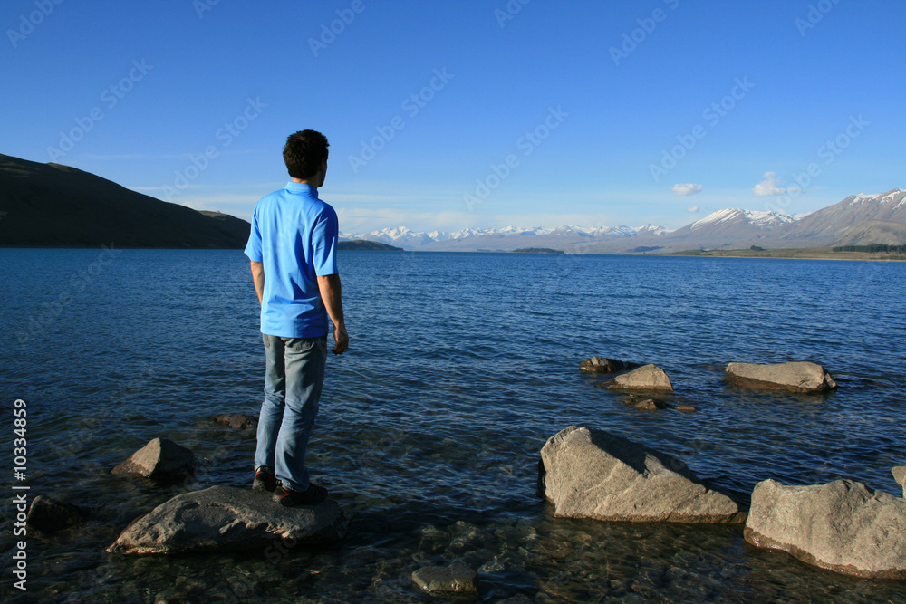 A man on a rock overlooking a rich blue lake