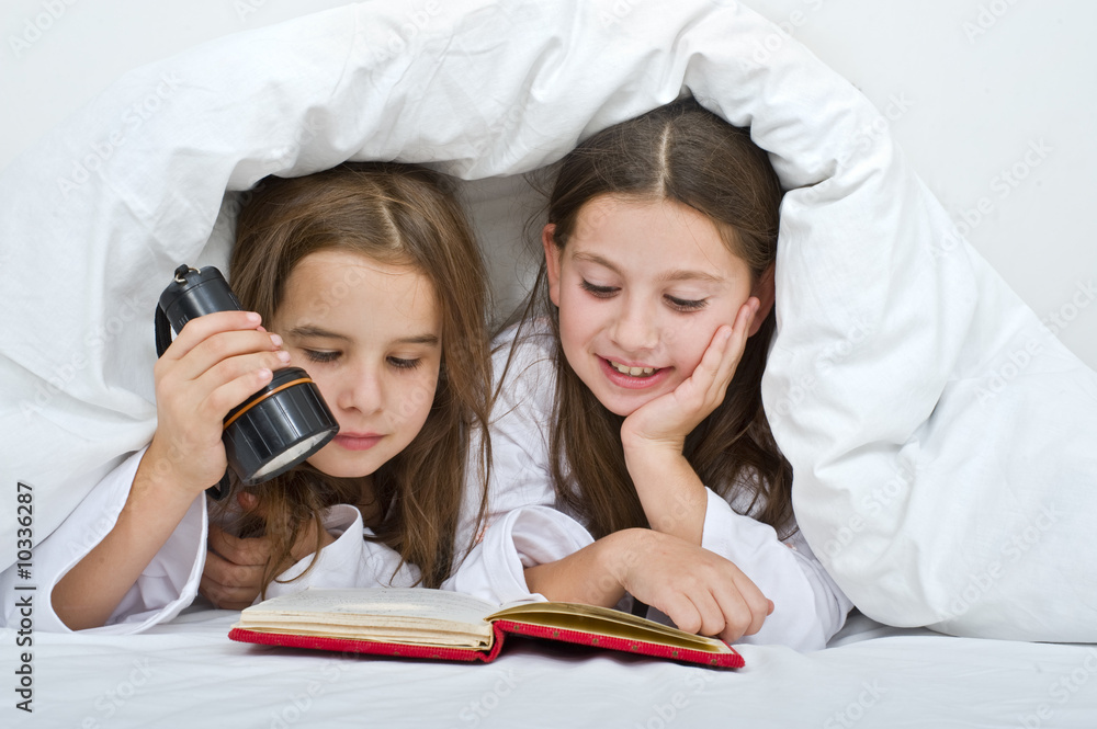 two girls reading under blanket with flashlight two girls reading under blanket with flashlight