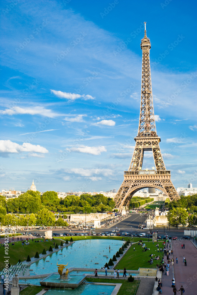 Naklejka premium Eiffel Tower, with cloudy blue sky and sunny trees around.