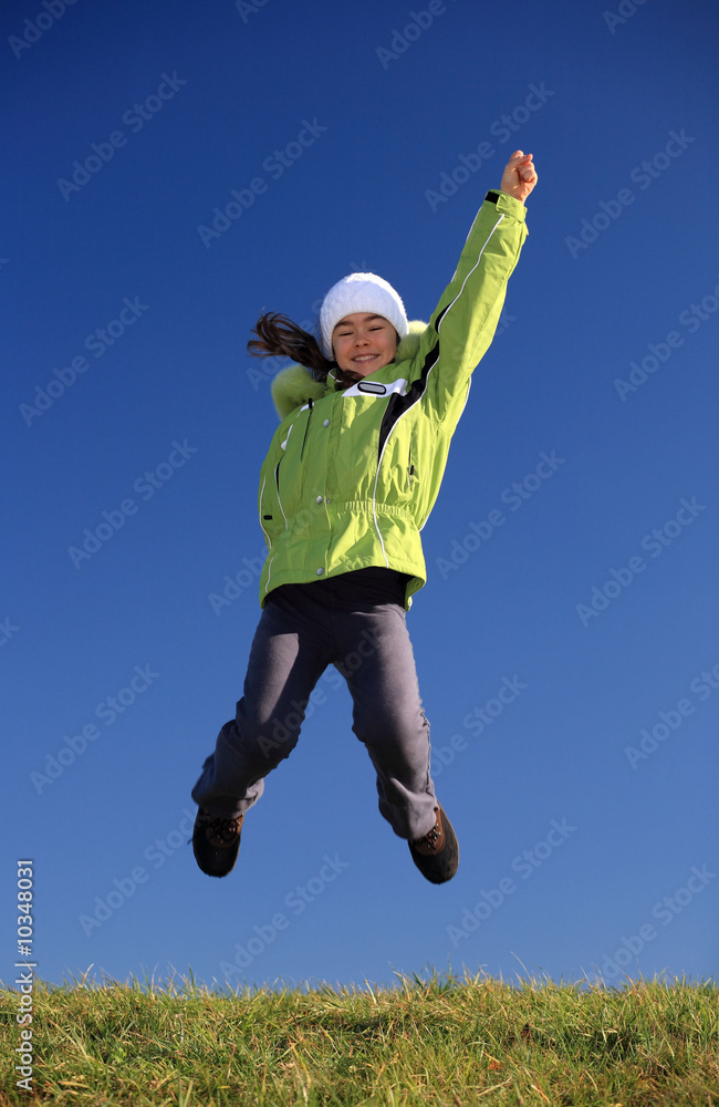 Young girl wearing winter jacket jumping against blue sky Young girl wearing winter jacket jumping against blue sky