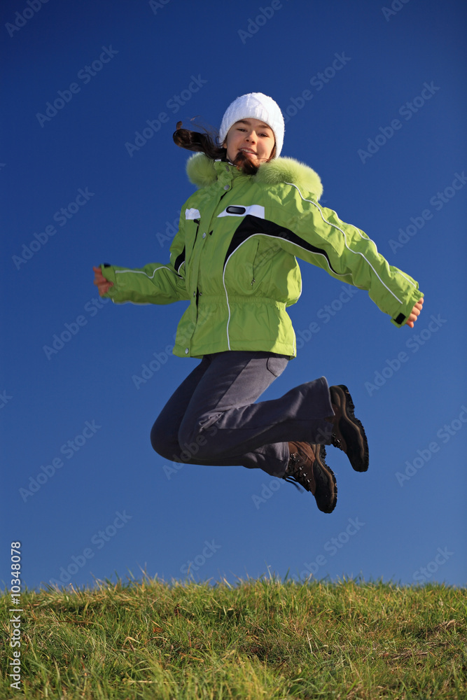 Young girl wearing winter jacket jumping against blue sky Young girl wearing winter jacket jumping against blue sky