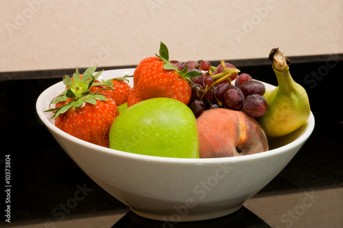 Close up of white fruit bowl with apple, strawberries, banana