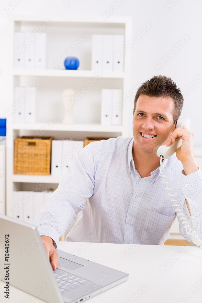 Business man working on computer at home calling on phone Business man working on computer at home calling on phone