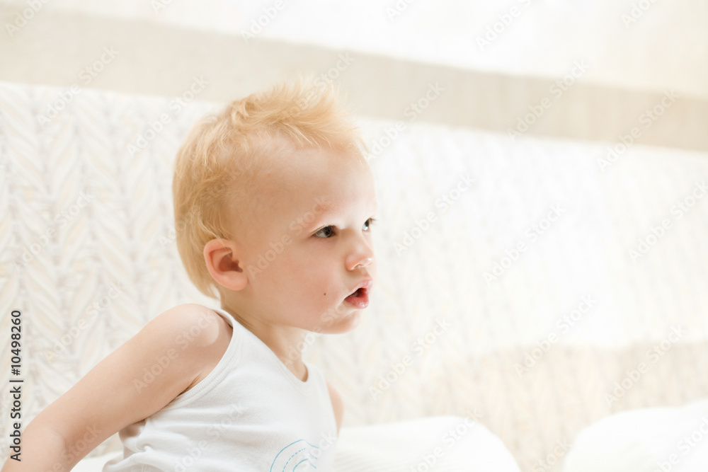 Pensive little boy sitting on white sofa at home Pensive little boy sitting on white sofa at home