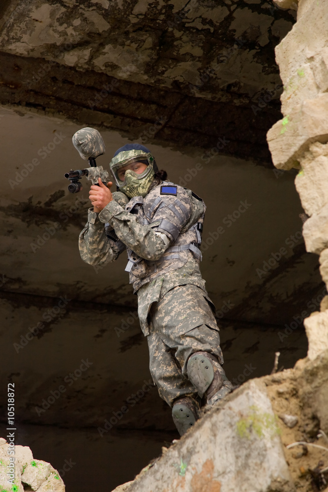 Fototapeta premium Paintball player in camouflage uniform hiding in abandoned place