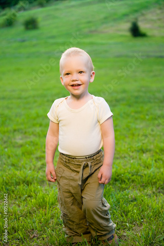 Portrait of smiling little boy on sunny green grass field © Igor Stepovik