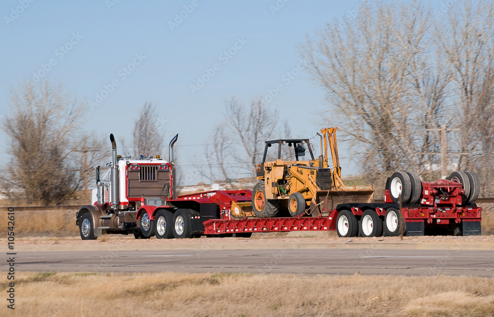Semi-truck pulling a loaded drop-deck trailer. Semi-truck pulling a loaded drop-deck trailer.