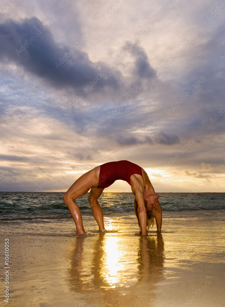 woman doing yoga and stretches on the beach at sunrise.