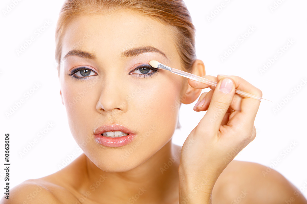 Portrait of beautiful blond woman doing makeup, on white