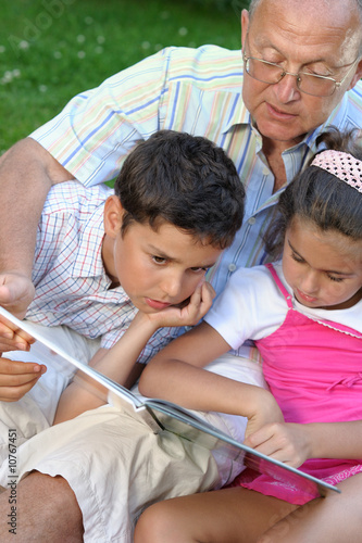 Grandfather and kids reading book outdoors