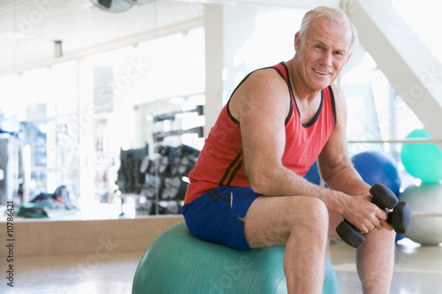 Man Using Hand Weights On Swiss Ball At Gym