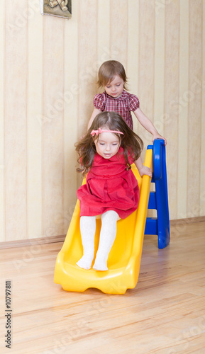 Two adorable girls having fun atop playground slide