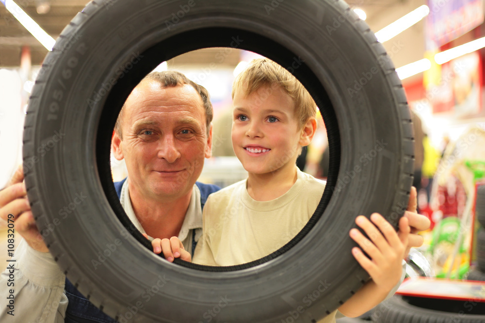 Boy and man look into vehicle tire in store Boy and man look into vehicle tire in store